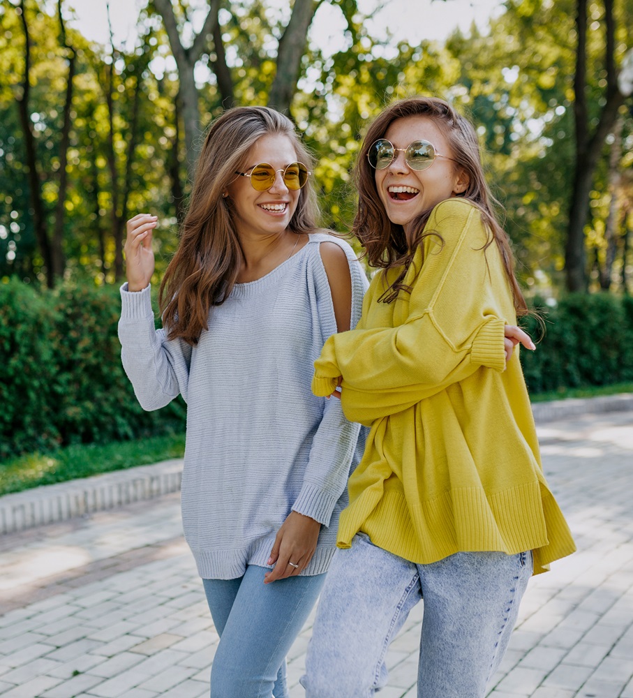 Two women smiling and enjoying a walk outdoors while wearing sunglasses - Optometrist Chapel Hill Two women smiling and enjoying a walk outdoors while wearing sunglasses - Optometrist Chapel Hill