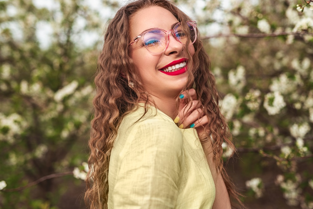 A woman smiling while wearing glasses in front of blooming trees - Optometrist Chapel Hill A woman smiling while wearing glasses in front of blooming trees - Optometrist Chapel Hill